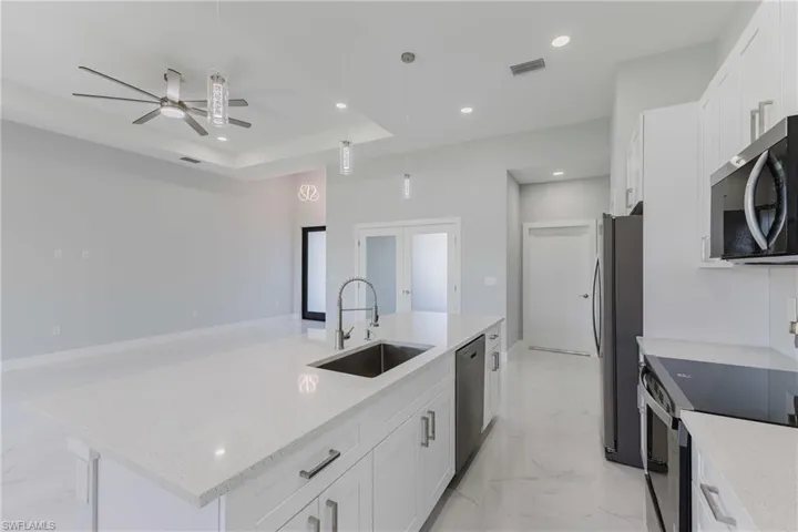 Kitchen with an island with sink, white cabinetry, stainless steel appliances, light stone countertops, and a raised ceiling