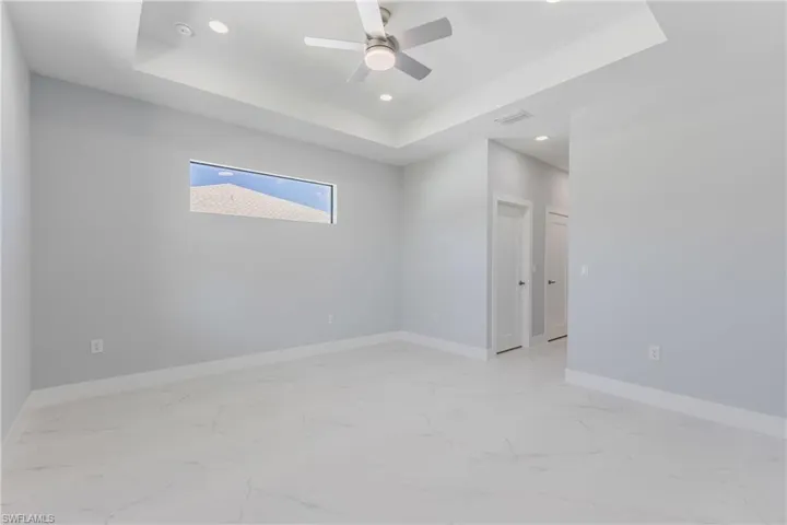 Spare room with a raised ceiling, light marble finish floors, ceiling fan, and recessed lighting