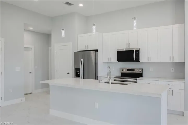 Kitchen with stainless steel appliances, light stone countertops, light marble finish flooring, white cabinetry, and a kitchen island with sink