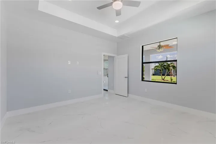Empty room with light marble finish flooring, ceiling fan, recessed lighting, and a tray ceiling