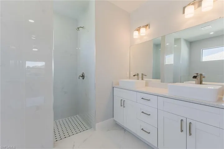 Bathroom featuring a marble finish shower, double vanity, and light marble finish floors