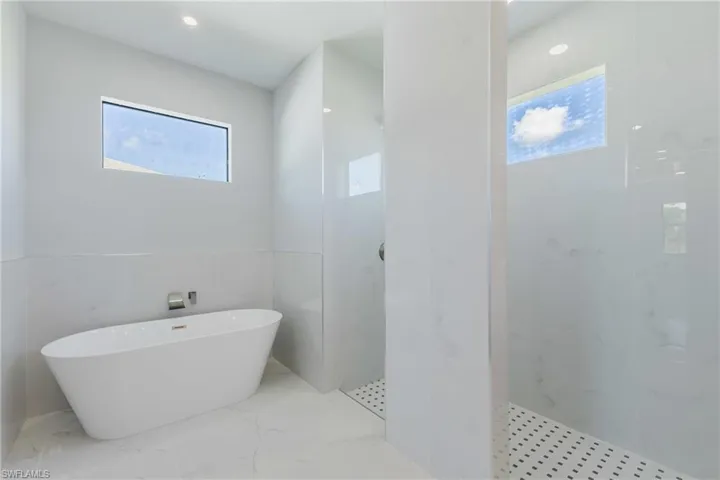 Bathroom with a soaking tub, a marble finish shower, wainscoting, light marble finish floors, and recessed lighting