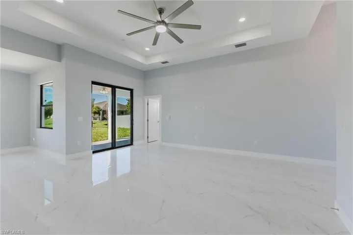 Empty room featuring a tray ceiling, a ceiling fan, recessed lighting, and light marble finish flooring