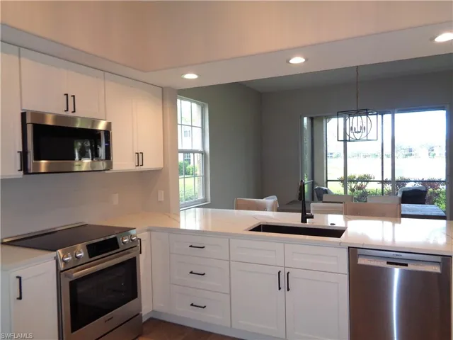Kitchen featuring stainless steel appliances, white cabinetry, light stone counters, suspended lighting, and a peninsula