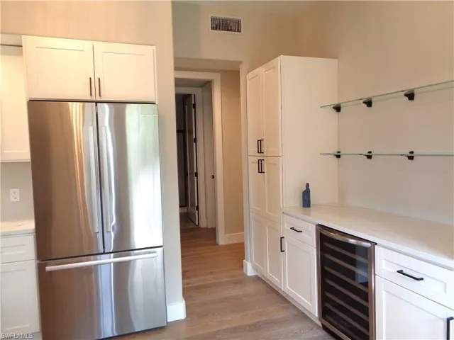 Bar area featuring freestanding refrigerator, white cabinetry, beverage cooler, light wood-type flooring, and light stone counters