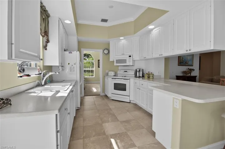 Kitchen featuring a peninsula, white cabinetry, ornamental molding, white appliances, and light countertops