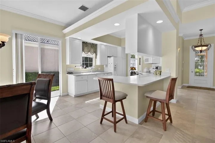 Kitchen with ornamental molding, a kitchen breakfast bar, a peninsula, light countertops, and white cabinetry
