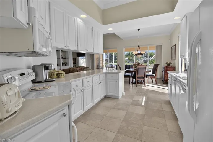 Kitchen with white appliances, ornamental molding, white cabinetry, a peninsula, and hanging lights