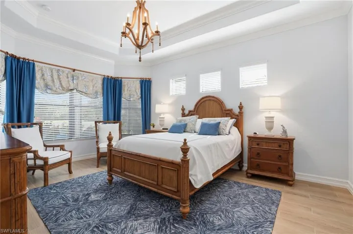 Bedroom with crown molding, light wood finished floors, a chandelier, multiple windows, and a raised ceiling