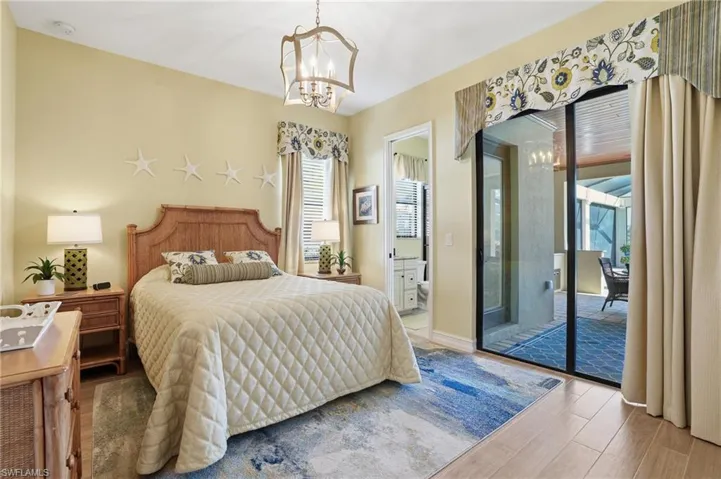 Bedroom with a chandelier, wood finished floors, access to outside, and ensuite bathroom