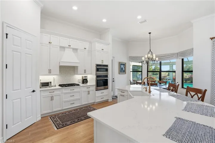 Kitchen featuring white cabinetry, decorative light fixtures, a chandelier, ornamental molding, and light wood-type flooring