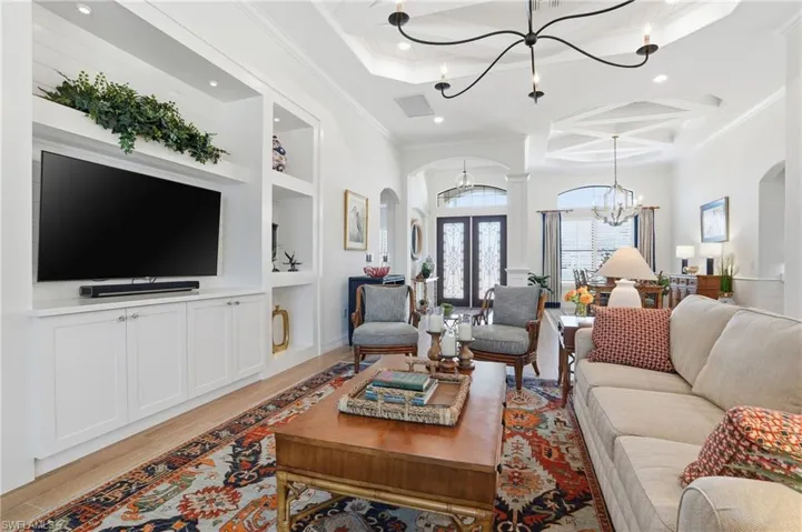 Living area with built in shelves, coffered ceiling, arched walkways, light wood-style floors, and a chandelier