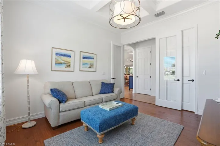 Living area with coffered ceiling, crown molding, dark wood-style flooring, arched walkways, and beam ceiling