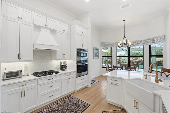 Kitchen with white cabinetry, a chandelier, custom exhaust hood, pendant lighting, and light stone counters