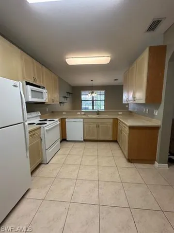 Kitchen with white appliances, light wood finish cabinets, light countertops, decorative light fixtures, and light tile patterned floors