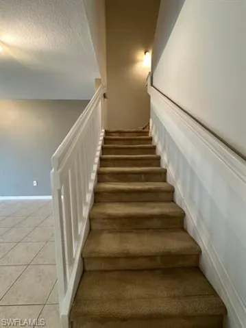 Stairway with tile patterned flooring and a textured ceiling
