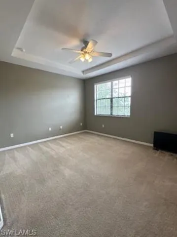 Carpeted spare room featuring a raised ceiling and a ceiling fan