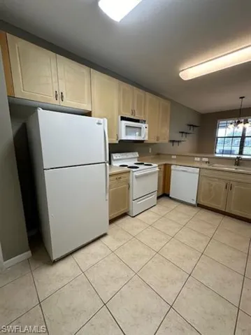 Kitchen with white appliances, light countertops, light tile patterned flooring, light wood finish cabinets, and suspended lighting
