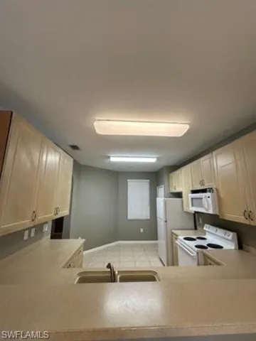 Kitchen with white appliances, light countertops, a peninsula, and light wood finish cabinets