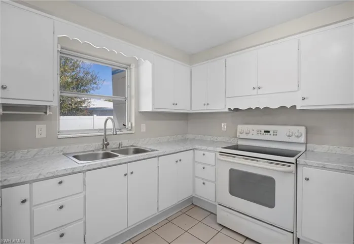 Kitchen featuring white electric range oven, light countertops, white cabinetry, light tile patterned flooring, and under cabinet range hood
