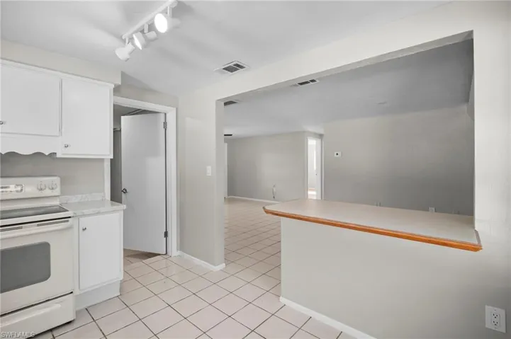 Kitchen featuring white electric range, light countertops, track lighting, white cabinetry, and light tile patterned floors