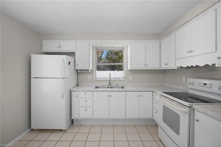 Kitchen featuring white appliances, light countertops, white cabinetry, and light tile patterned flooring
