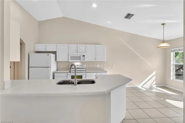 Kitchen with white appliances, a peninsula, lofted ceiling, white cabinets, and light tile patterned flooring