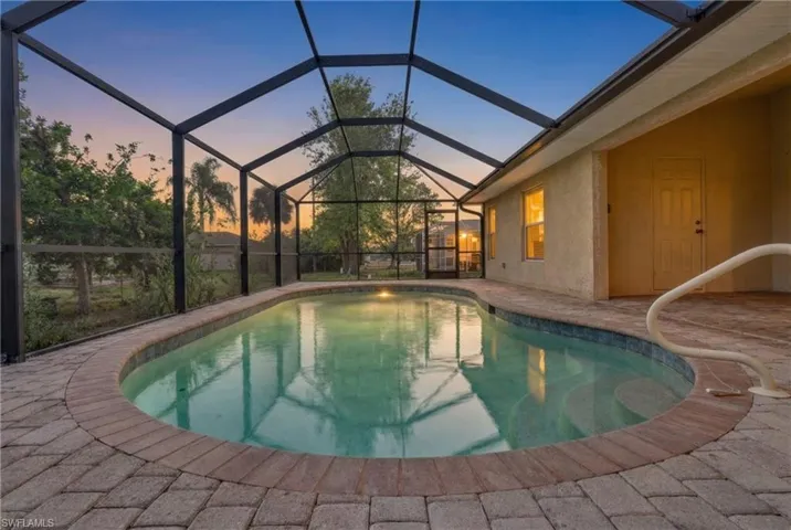 Pool at dusk with an outdoor pool, a sunroom, a patio area, and glass enclosure