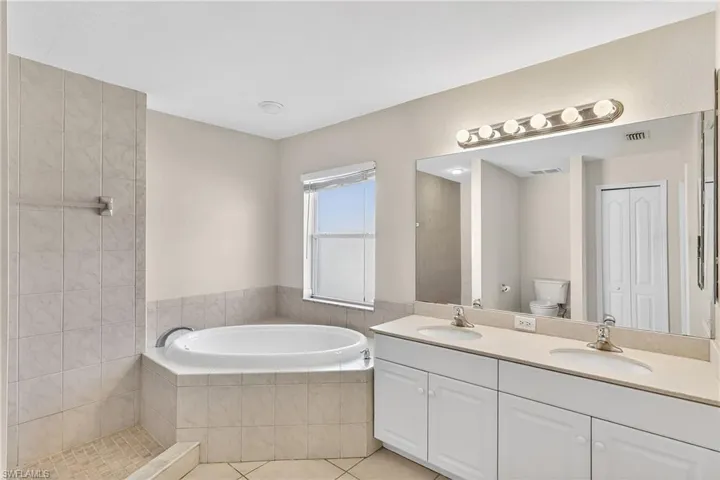 Full bathroom featuring double vanity, a garden tub, light tile patterned floors, and a closet
