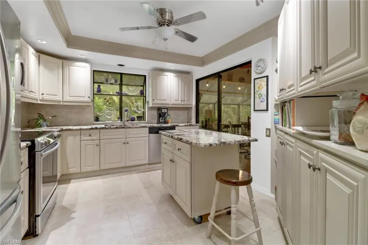Kitchen featuring appliances with stainless steel finishes, a kitchen breakfast bar, a tray ceiling, ceiling fan, and a kitchen island