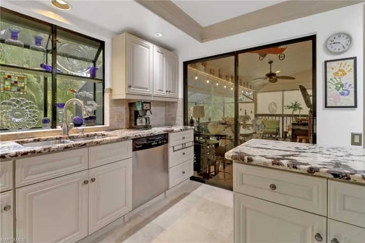 Kitchen with light stone countertops, backsplash, stainless steel dishwasher, ceiling fan, and sink