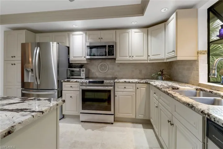 Kitchen with backsplash, light stone counters, sink, and stainless steel appliances