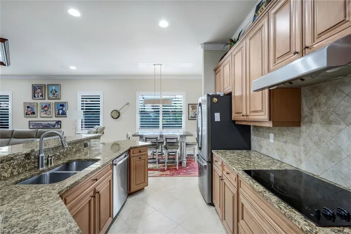 Kitchen with stainless steel appliances, light stone countertops, crown molding, under cabinet range hood, and pendant lighting