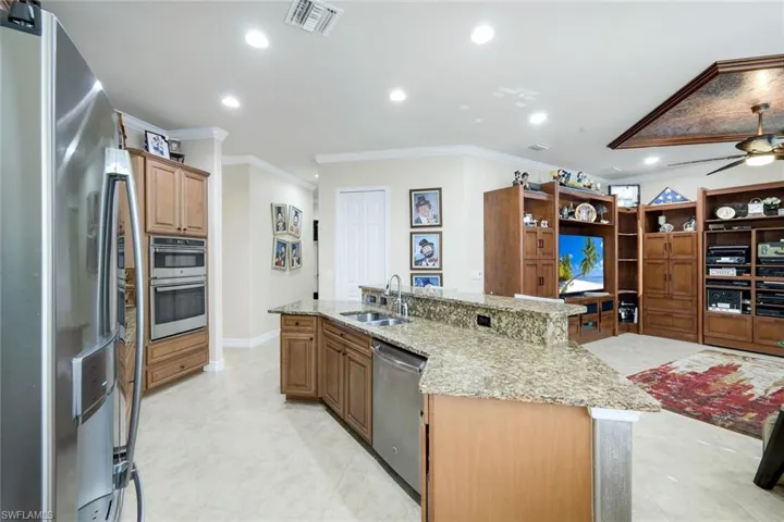 Kitchen with stainless steel appliances, a kitchen island with sink, crown molding, light stone counters, and a ceiling fan