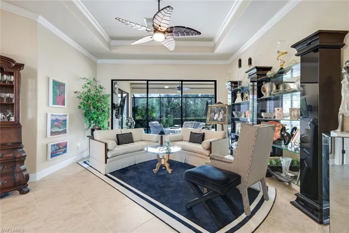 Living room featuring a raised ceiling, ornamental molding, light tile patterned flooring with sliding doors to covered lanai and pool