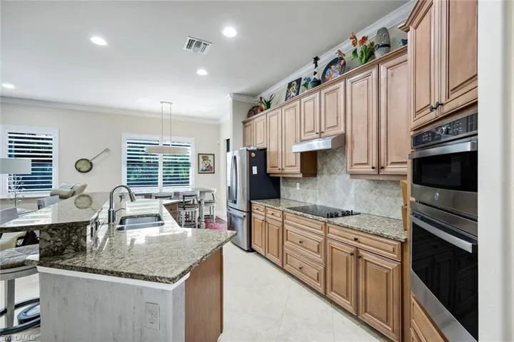 Kitchen featuring stainless steel appliances, light stone counters, ornamental molding, a breakfast bar, and decorative light fixtures