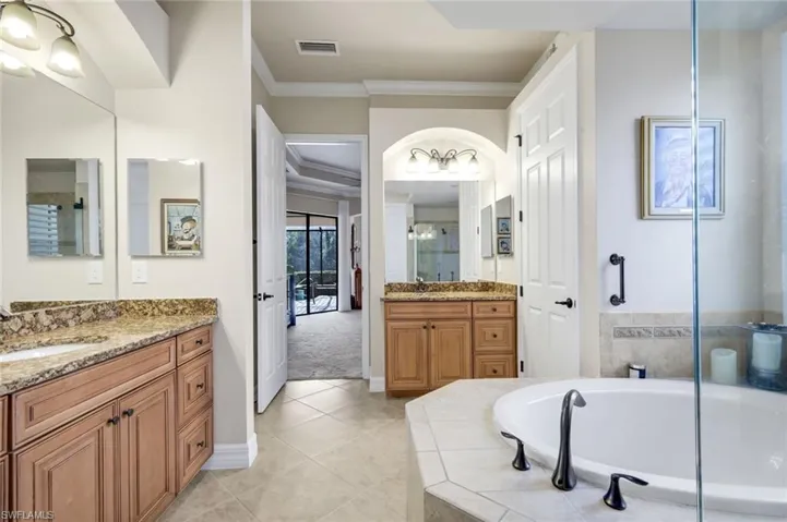 Bathroom with two vanities, crown molding, a garden tub, light tile patterned floors, and a shower stall