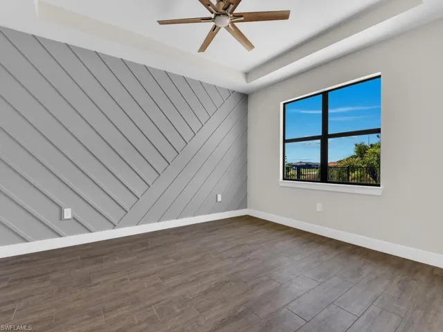 Spare room featuring a tray ceiling, baseboards, ceiling fan, and dark wood finished floors
