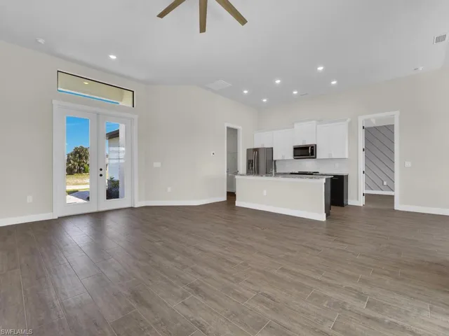 Unfurnished living room featuring dark wood finished floors, ceiling fan, baseboards, and french doors