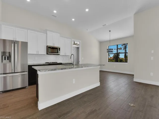 Kitchen with a sink, decorative backsplash, an island with sink, white cabinetry, and appliances with stainless steel finishes