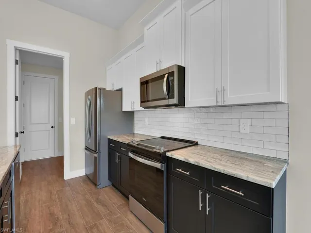 Kitchen with stainless steel appliances, wood finished floors, decorative backsplash, and white cabinetry