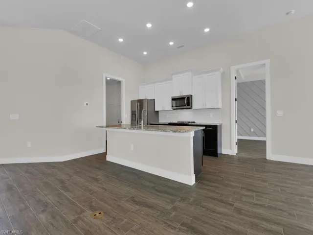 Kitchen with dark wood finished floors, tasteful backsplash, an island with sink, white cabinets, and appliances with stainless steel finishes