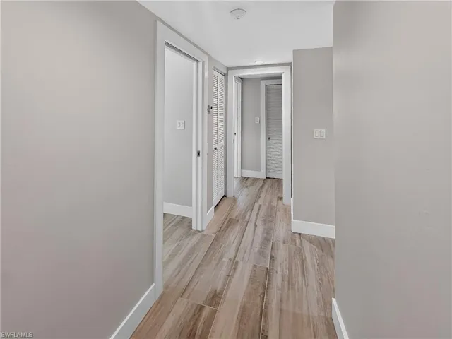 Hallway featuring wood-finish flooring, light grey painted walls, white trim, and multiple doorways