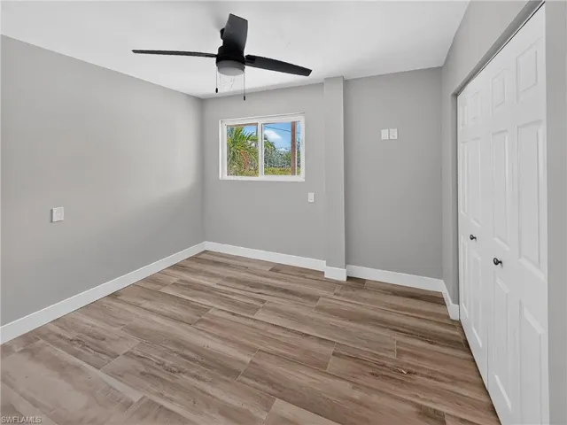 Room featuring wood-finish flooring, a ceiling fan, a window, bifold closet doors, and light gray wall paint