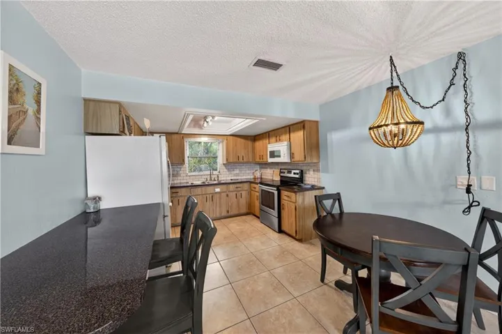 Kitchen and dining area featuring a breakfast bar with dark countertops, wood cabinetry, a tile backsplash, and stainless steel appliances