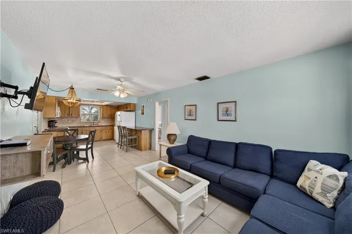 Open-concept living space featuring light-colored tile flooring, a kitchen with wood cabinetry and tile backsplash, and a breakfast bar