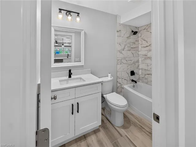 Full bathroom featuring a white vanity with integrated sink, matte black faucet, and a three-light fixture