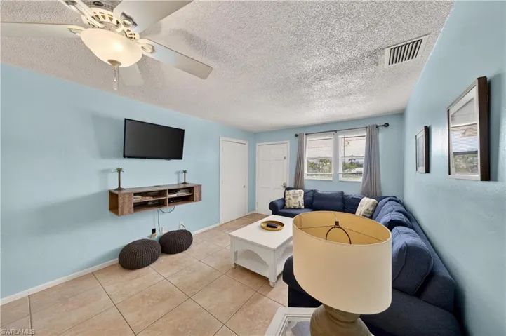 Living area featuring light blue walls, tile flooring, a ceiling fan with light fixture, multiple windows, and a built-in floating media console