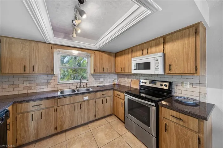 Kitchen featuring wood-finish cabinetry, dark countertops, tiled backsplash, stainless steel range, and a built-in microwave