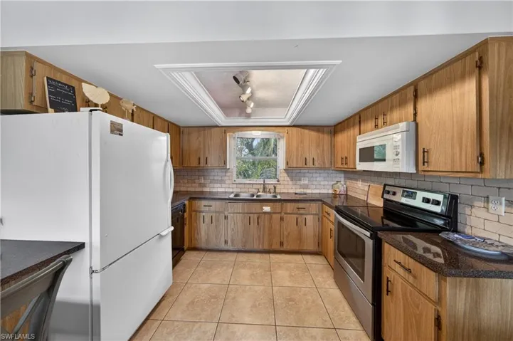 Kitchen featuring wood cabinetry, dark countertops, a tile backsplash, and tile flooring